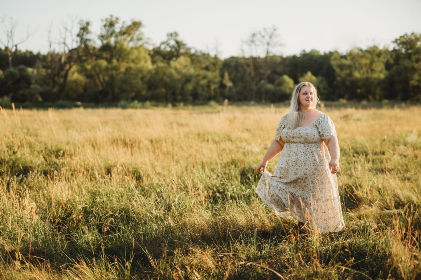 Frau mit blondem Haar in einem blumigen Kleid steht in einem Feld.